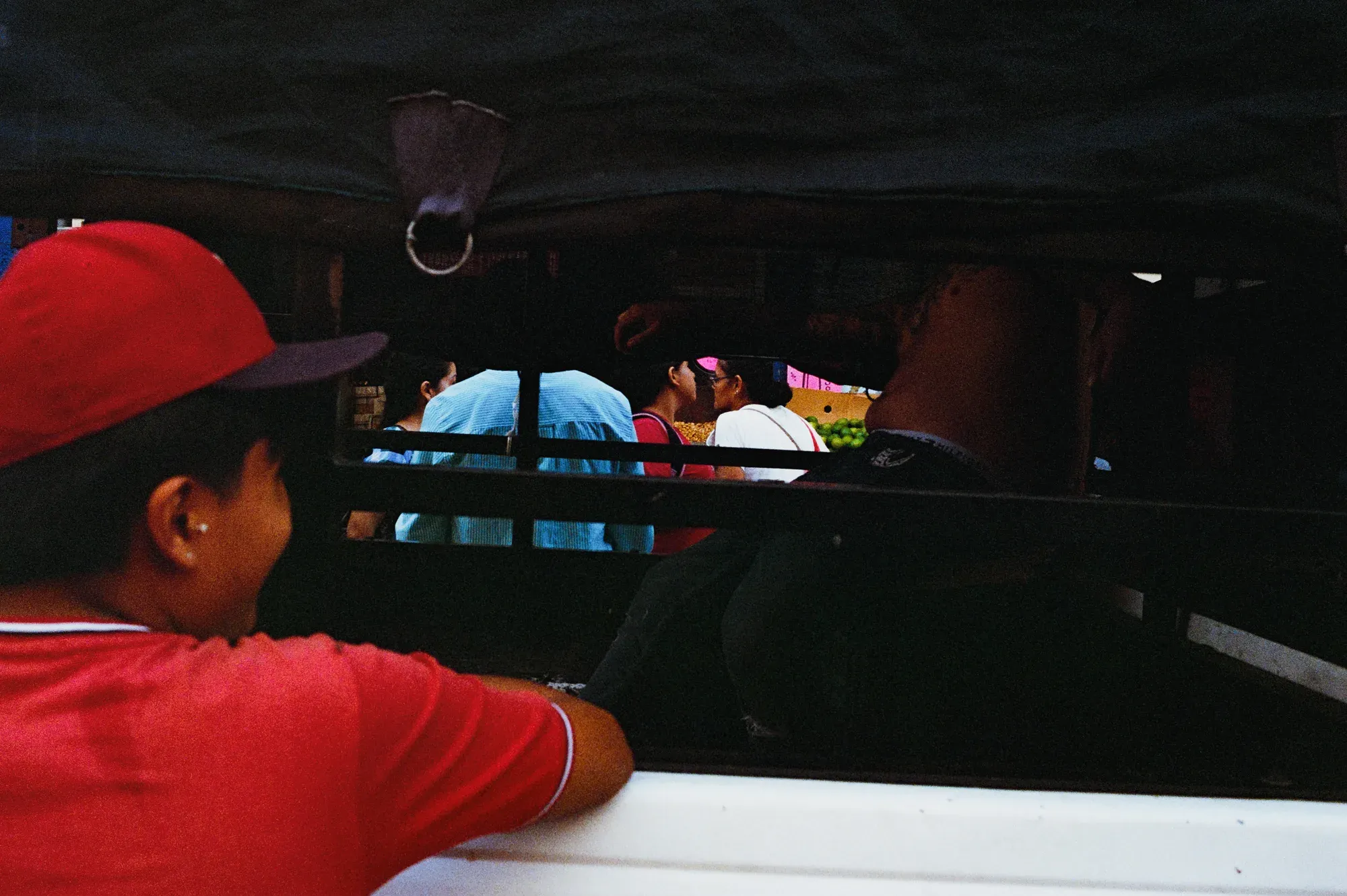 Niño de gorra y camiseta roja mira hacia la luz desde la sombra de una camioneta