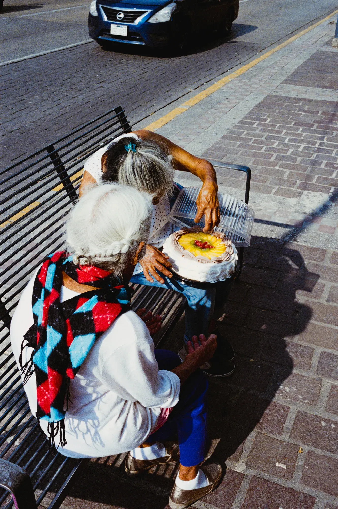 Dos mujeres mayores sentadas en una banca de la calle abren la caja de un pastel