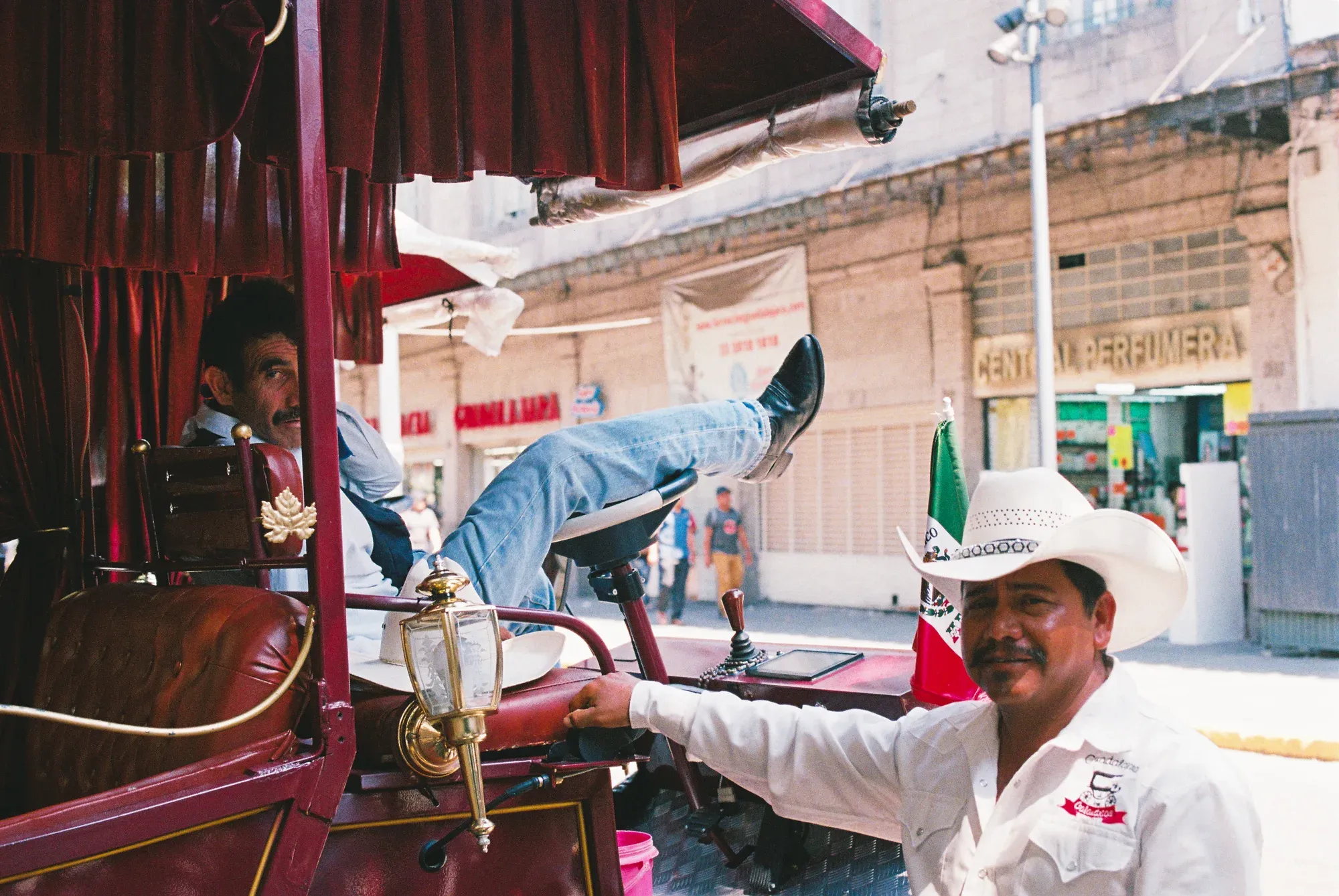 Hombre con sombrero vaquero junto a una calandria; dentro, otro hombre descansa con los pies sobre la ventana