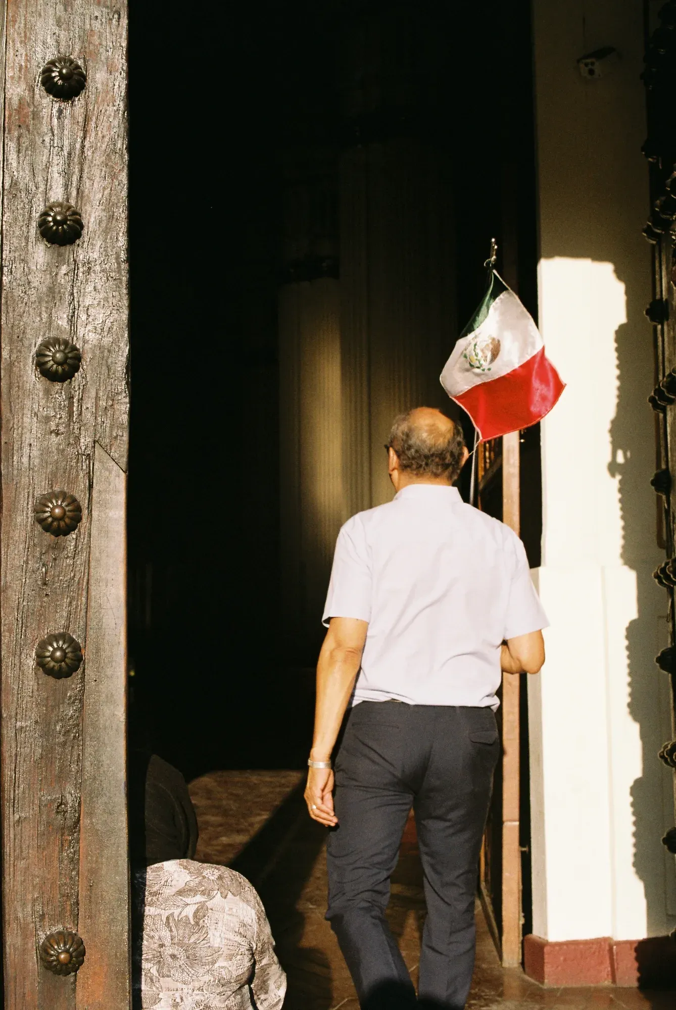 Hombre entra por el portón de un edificio junto a una bandera de México