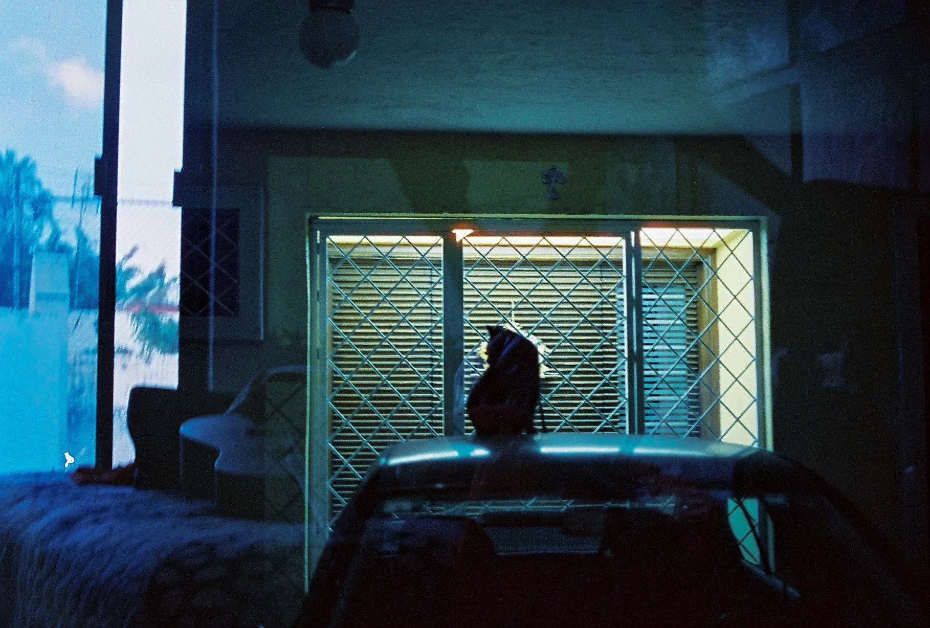 Fachada nocturna con luz verdosa y una silueta tras la reja de una ventana
