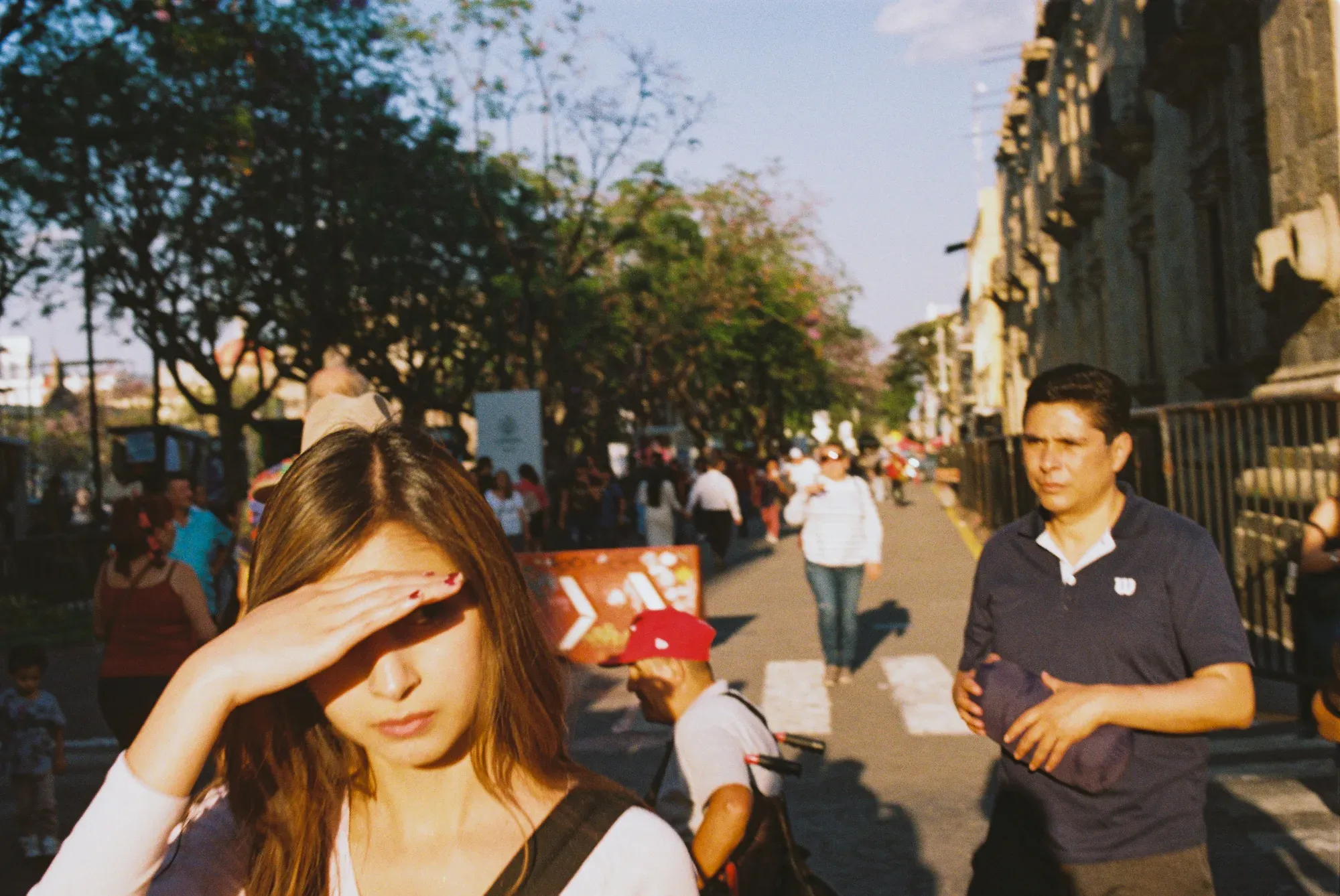 Mujer se cubre los ojos del sol en una avenida del centro, entre gente caminando