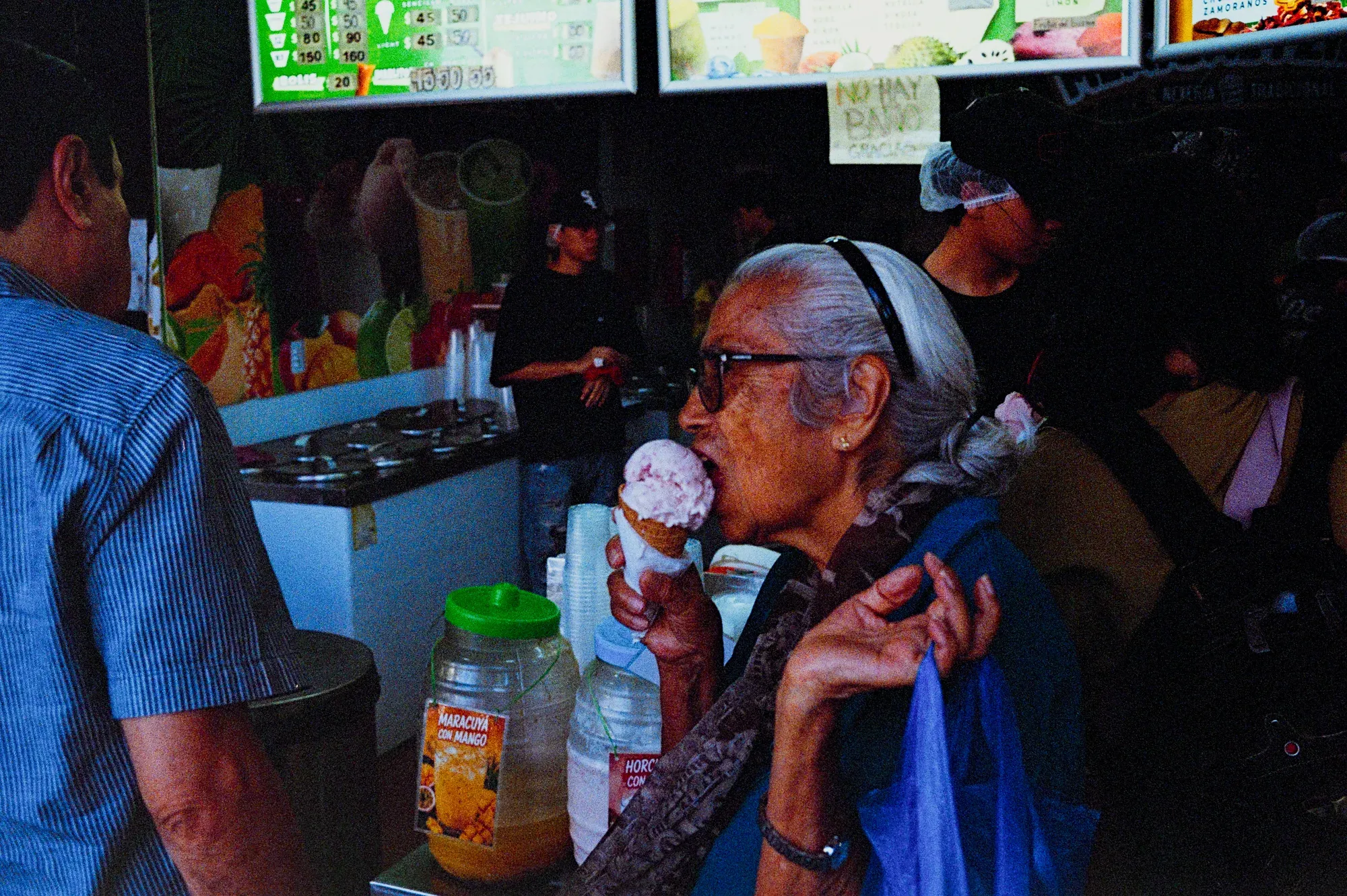 Mujer mayor come un helado de cono frente a un puesto de jugos