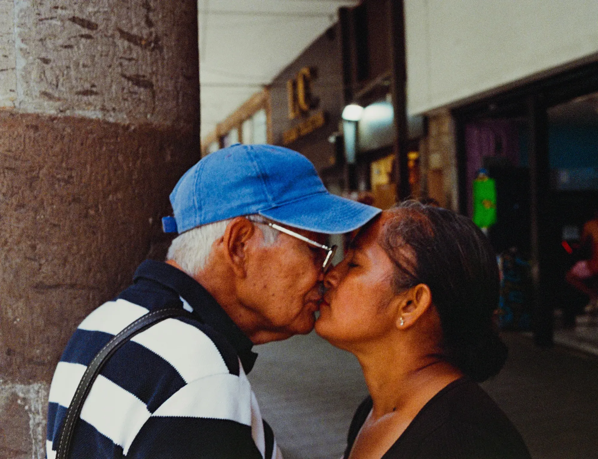 Hombre mayor de gorra azul besa a una mujer en un portal de la calle