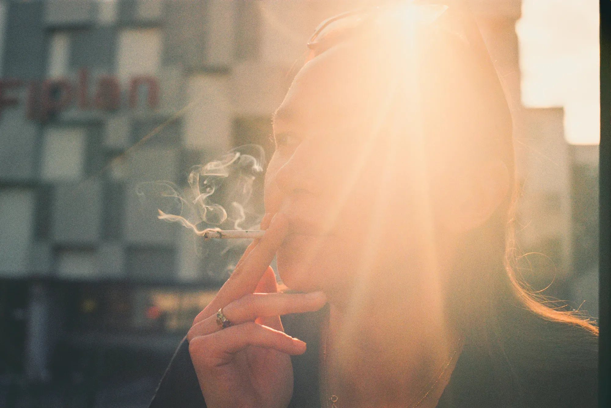 Mujer fuma a contraluz; el sol atraviesa el humo del cigarro