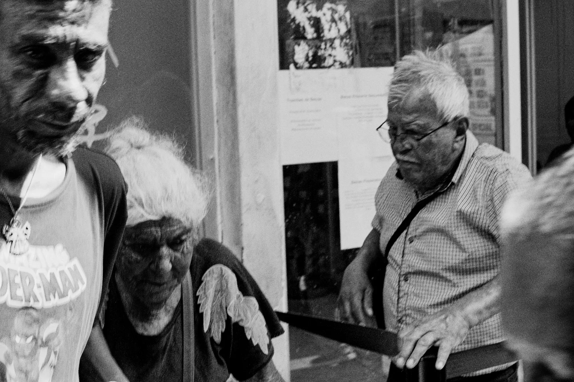 Blanco y negro: tres hombres a la entrada de un local; uno lleva una camiseta con alas dibujadas