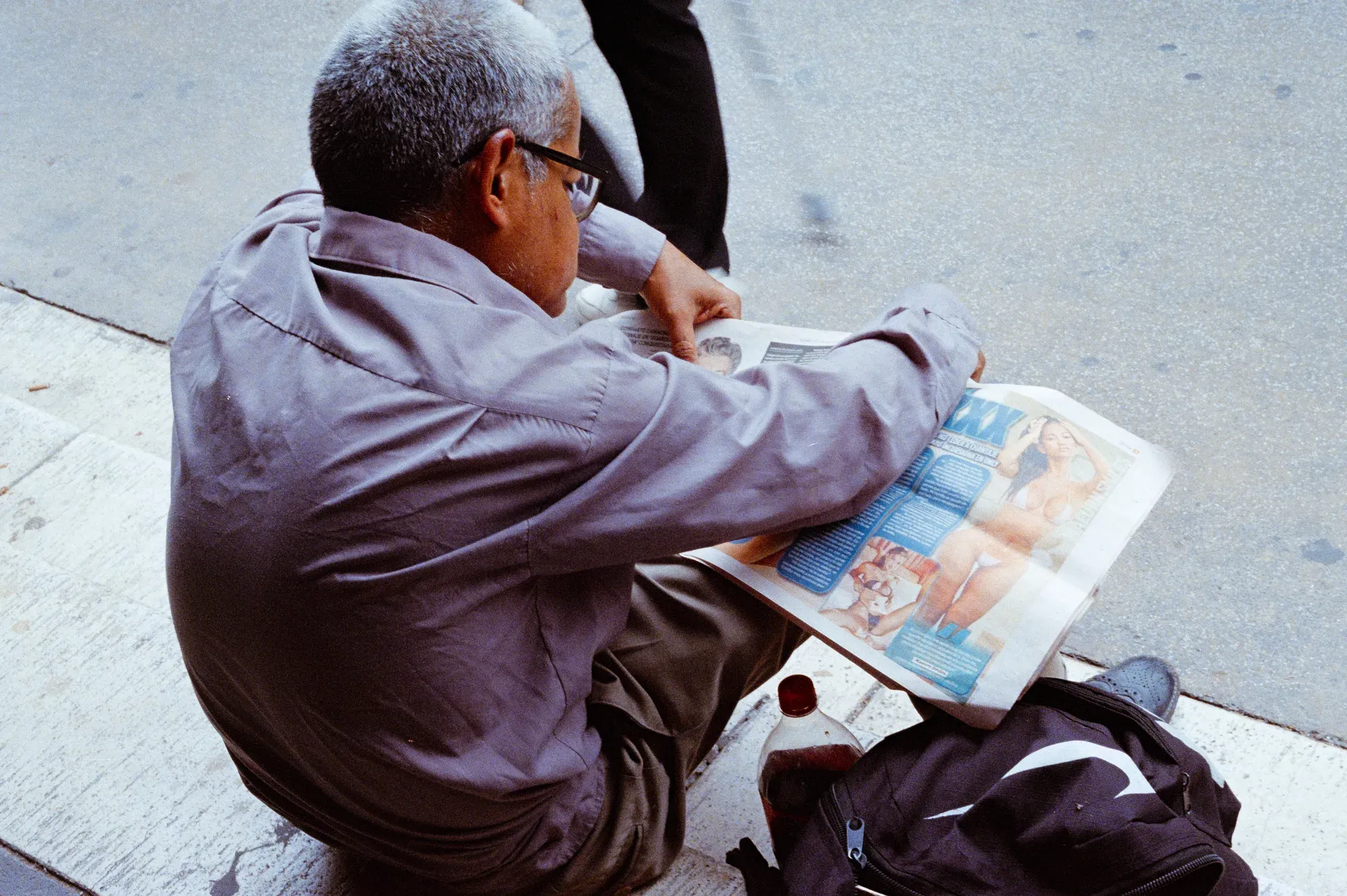 Hombre sentado en la banqueta lee un periódico abierto