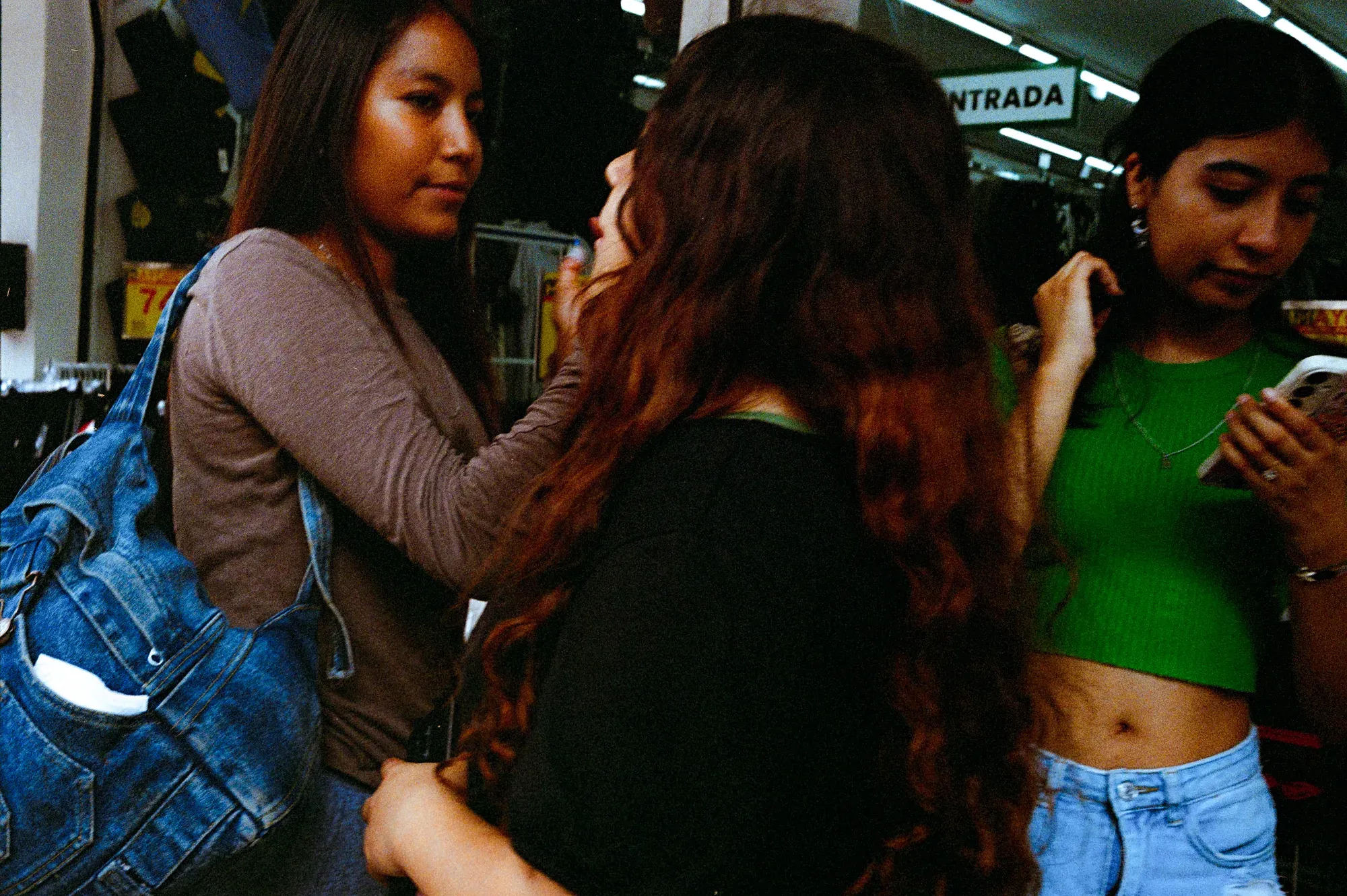 Tres mujeres jóvenes dentro de una tienda; una le acomoda el cabello a otra