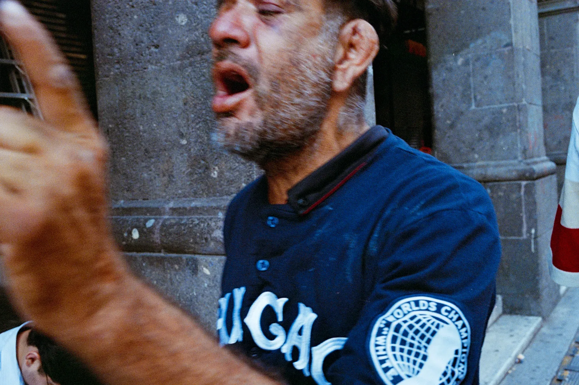 Primer plano de un hombre cantando con la boca abierta, con jersey azul de béisbol