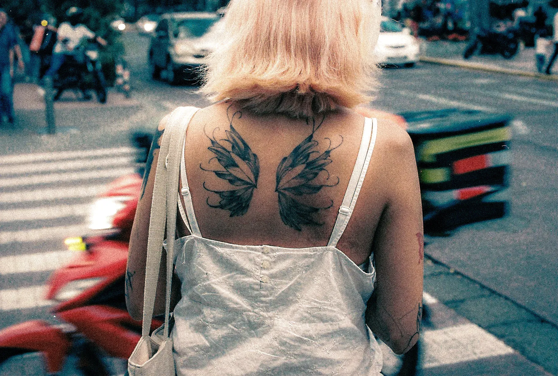 Mujer de espaldas con un tatuaje de alas en la espalda, en un cruce peatonal